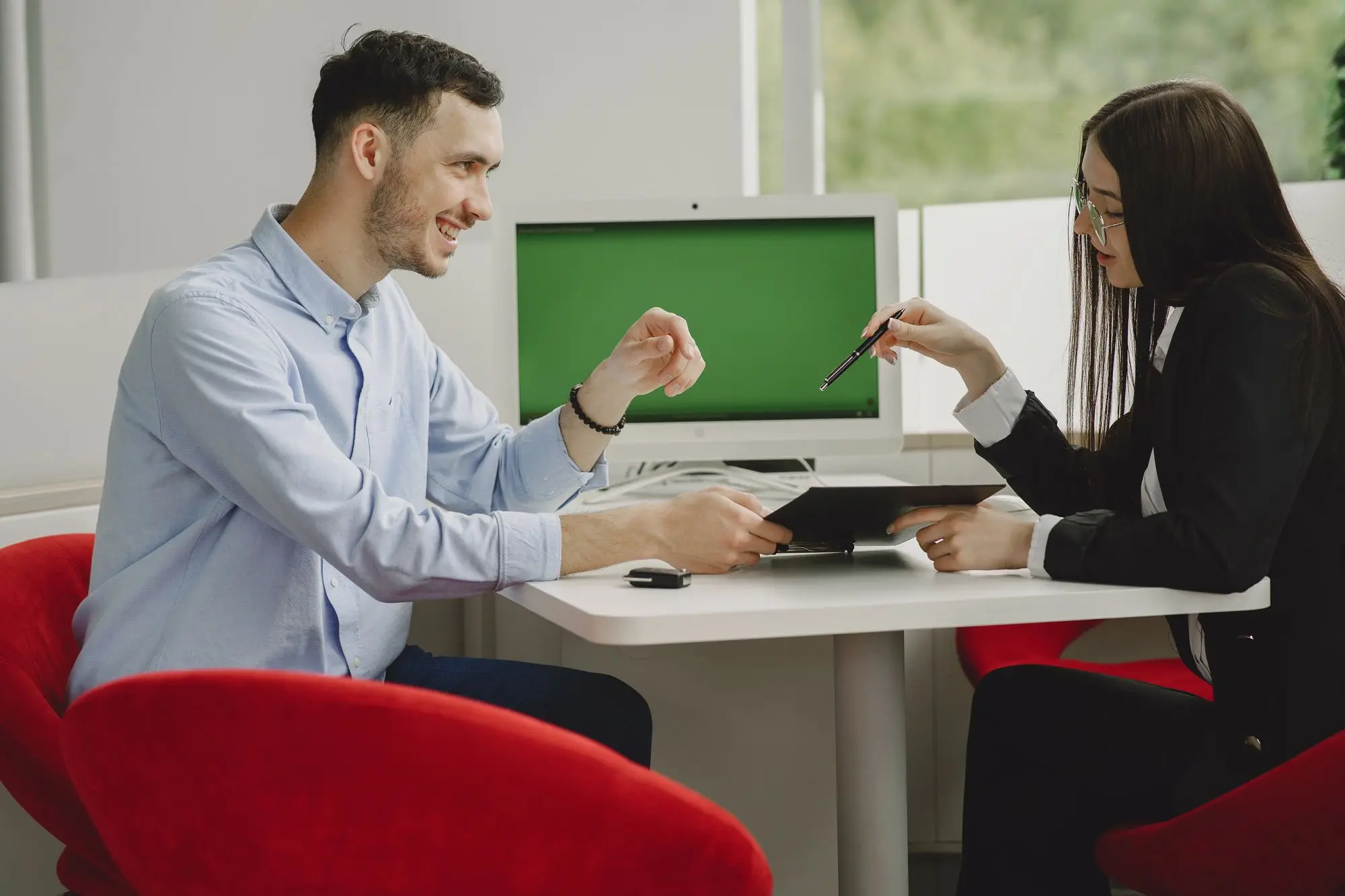 Business owner sitting across a branch desk from his bank lending officer, talking through a loan proposal on a tablet