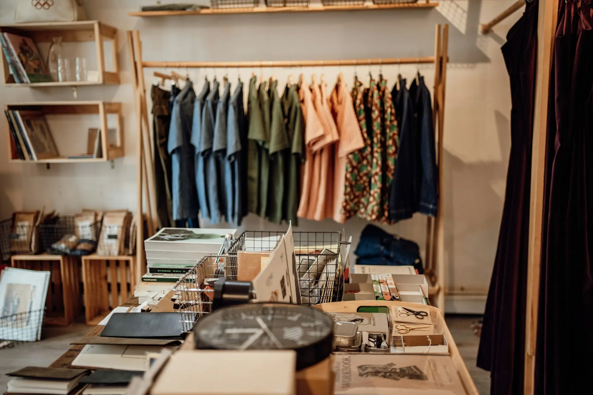 Racks of shirts and dresses above a display table of books, stationery and a wall clock in a small independent clothing boutique, the kind of seasonal stock an overdraft often funds